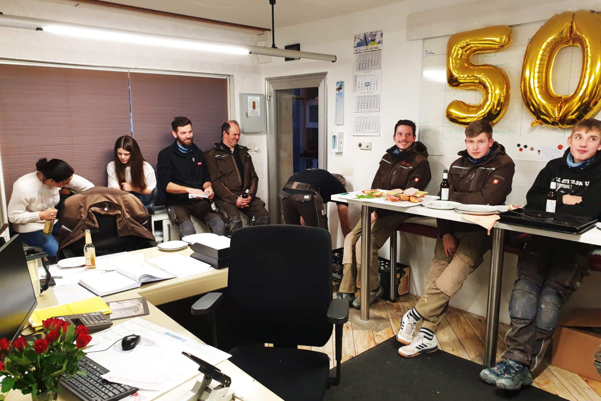 Mitarbeiter sitzen im Büro zusammen und feiern das 50.Jubiläum