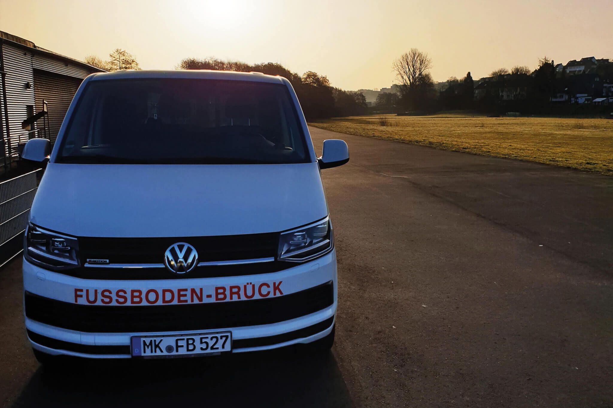 Firmenwagen steht neben Haus und Feld mit Sonnenuntergang